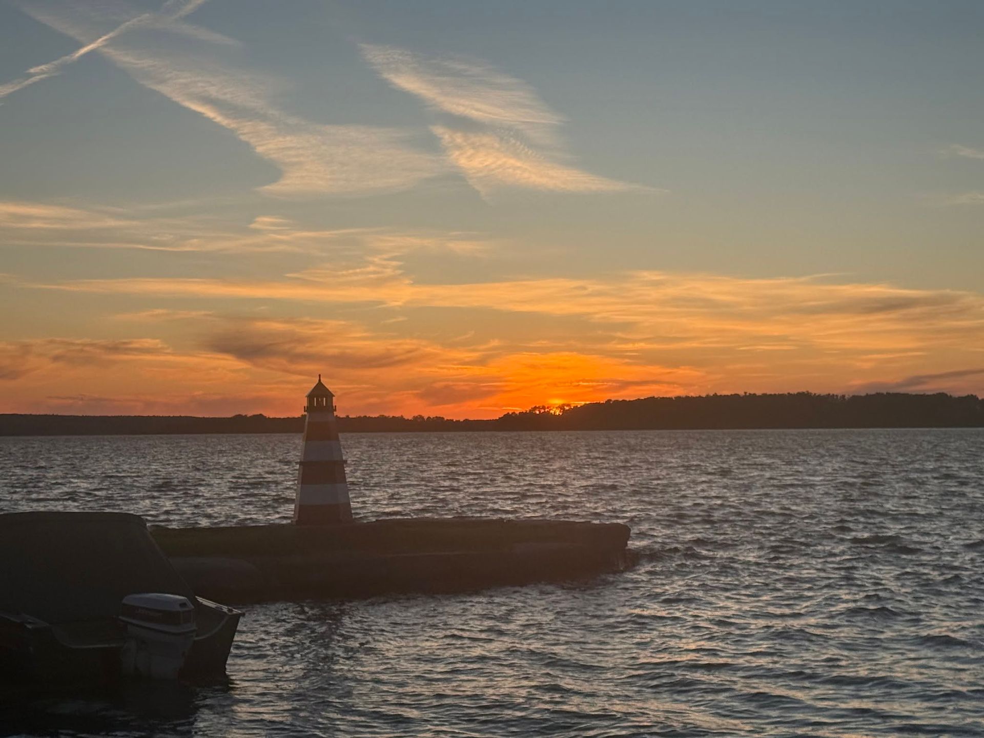 Sunset over choppy water with a lighthouse silhouette on a breakwater and orange clouds in the sky