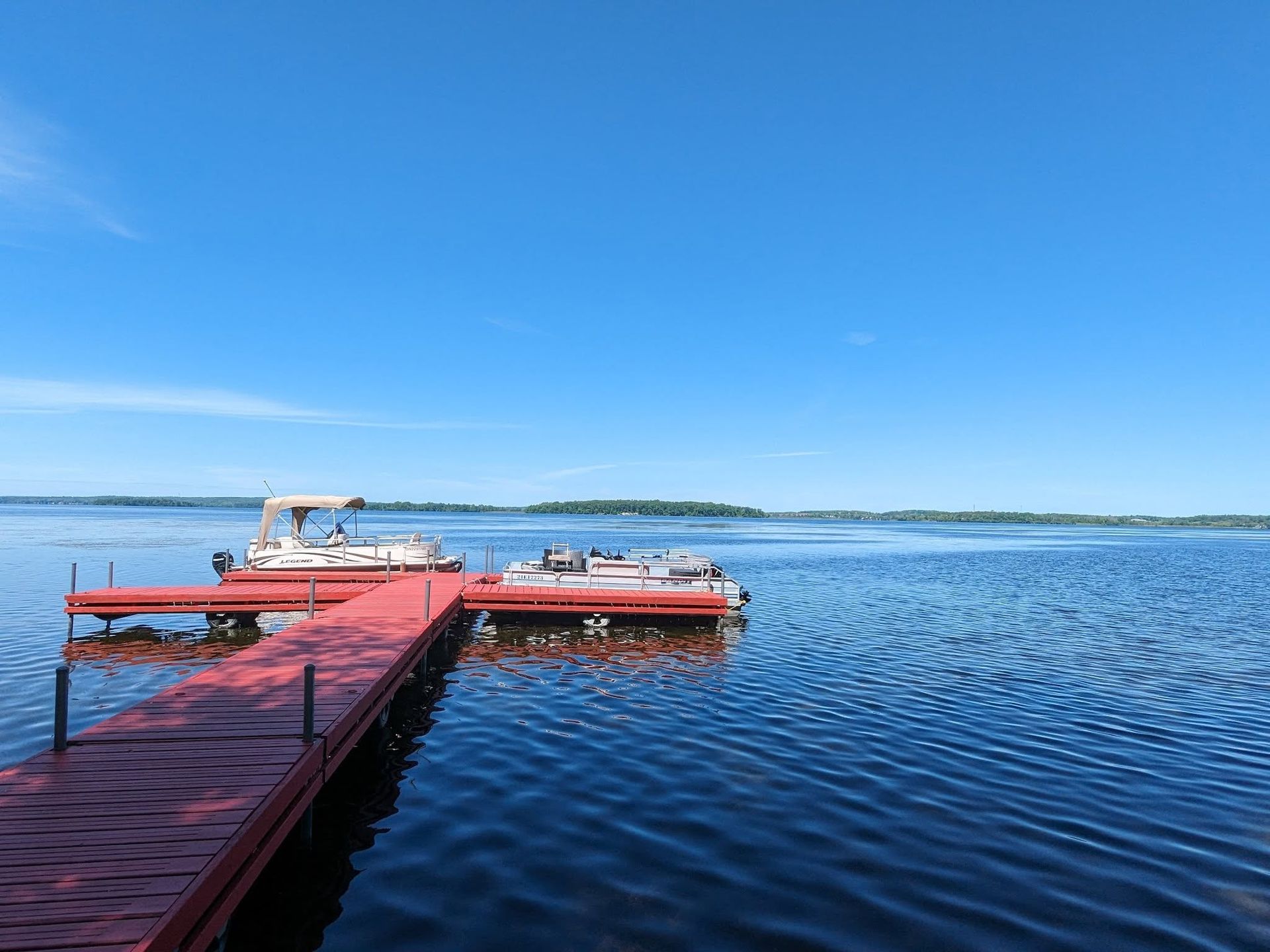 Red dock extending into a calm blue lake under a clear sky, with a small boat moored nearby