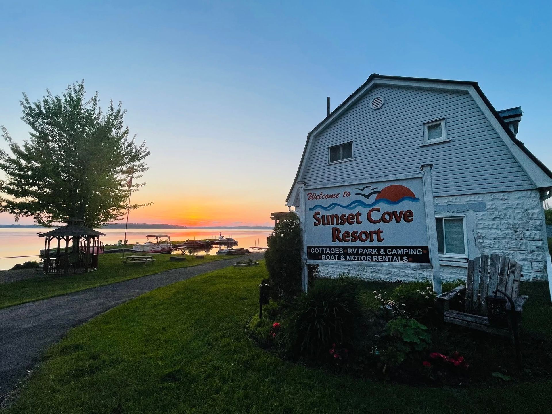 Sunset Cove Resort sign beside a white building at sunset by a lakeside path
