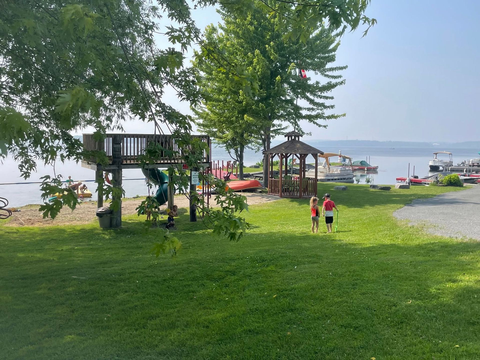 Park playground with a wooden play structure, people on grass, and a lake in the background