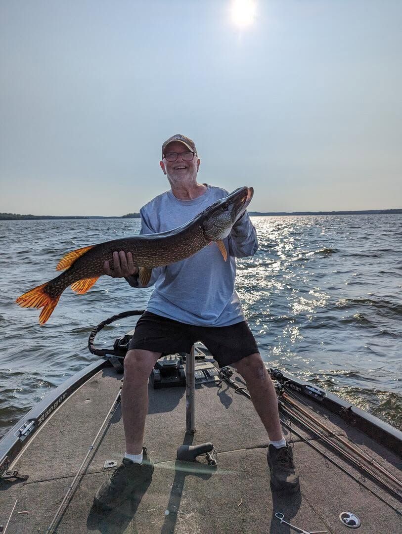 Person on a boat holding a large fish over the water at sunset