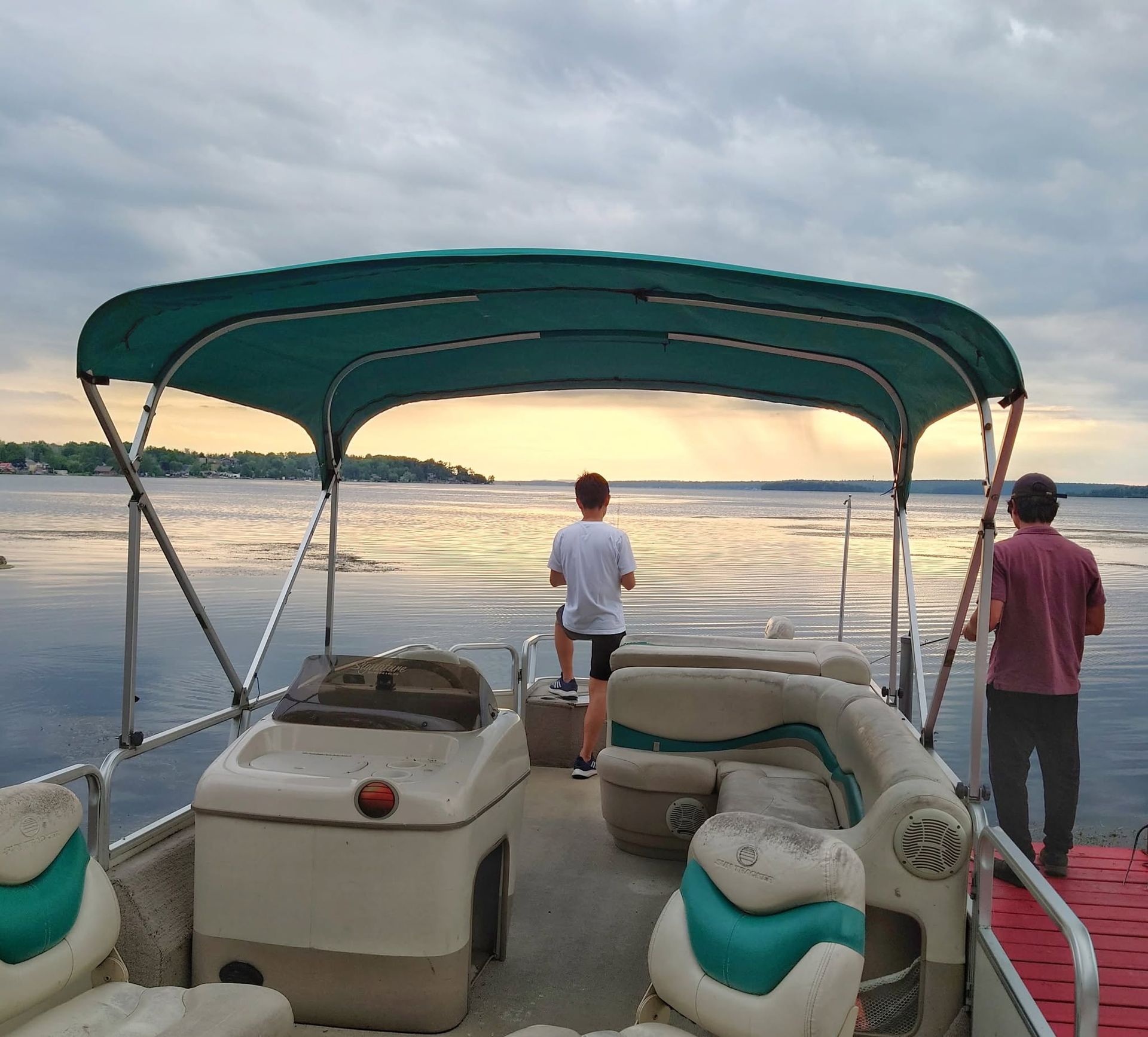 Pontoon boat at sunset with two people standing on the deck facing the water.