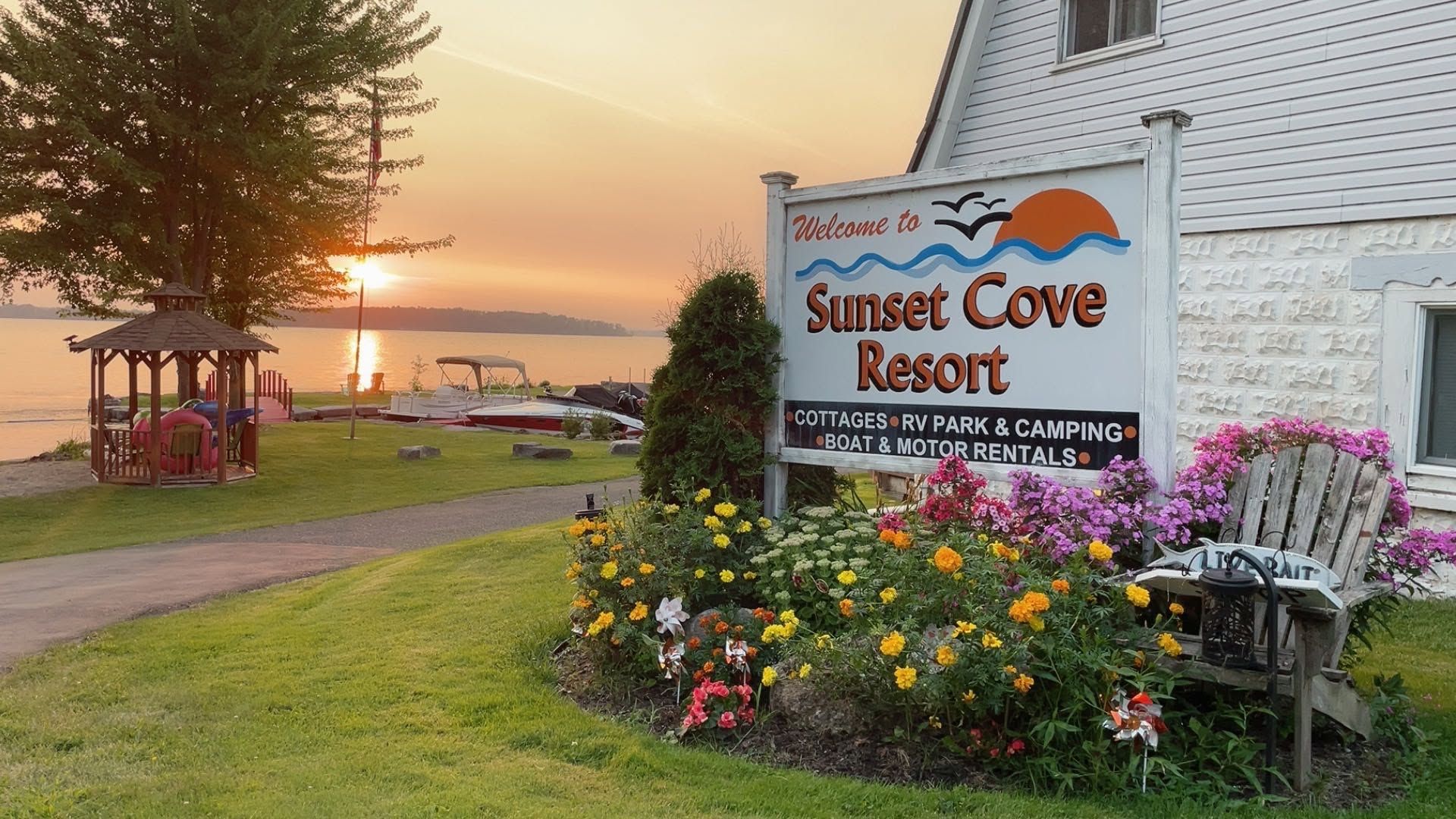 Sunset Cove Resort sign beside colorful flowers at sunset on a lakeside lawn