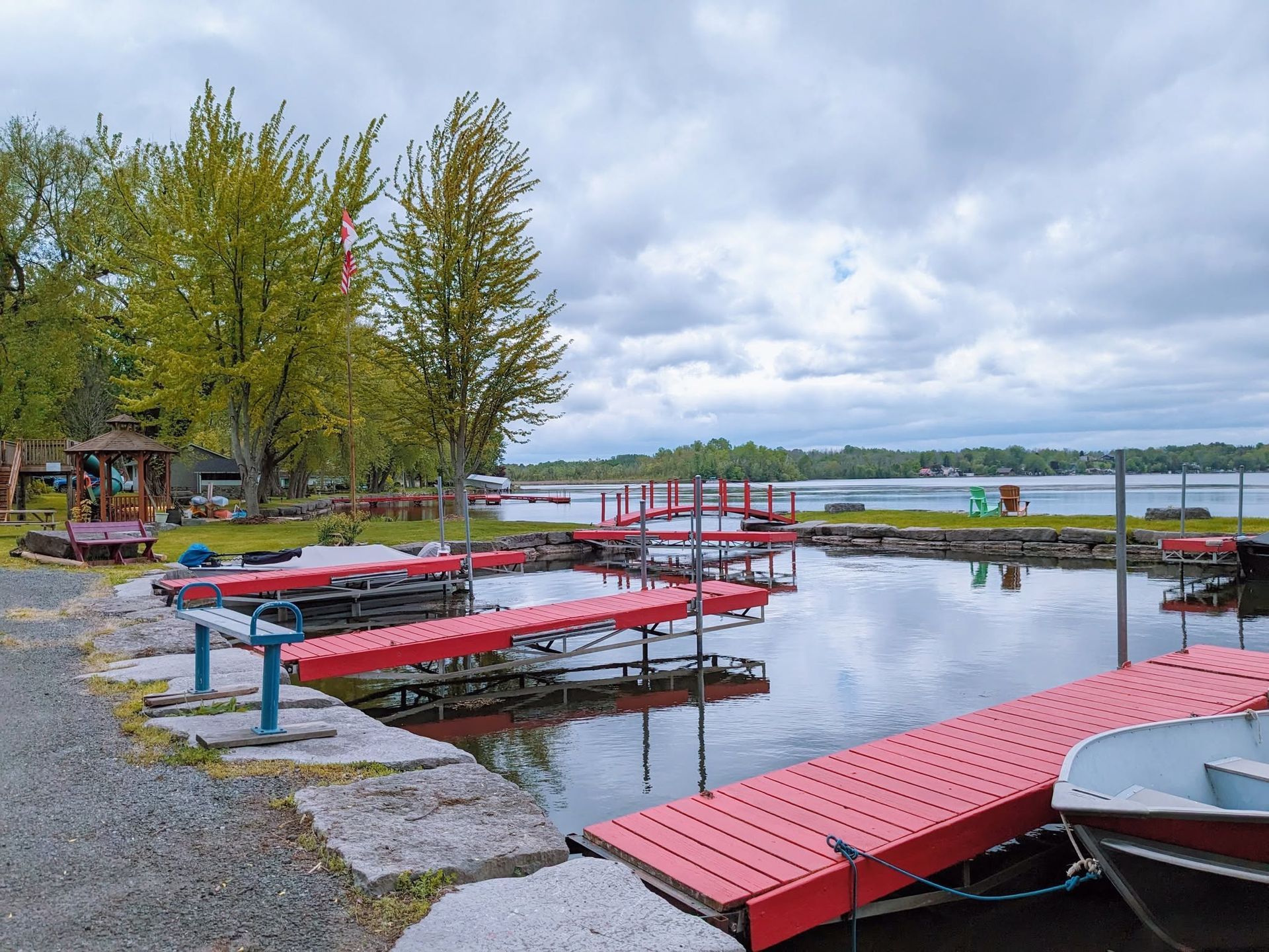 Small dock with red boats and floating platforms on a calm lakeside under cloudy skies