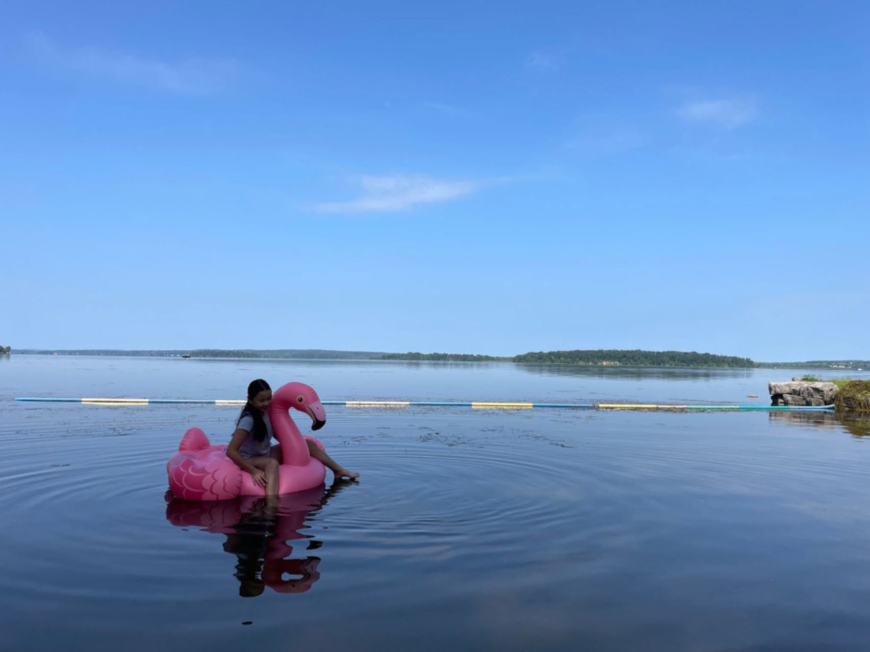 Person in a pink dress standing in shallow water by a calm blue lake under a clear sky