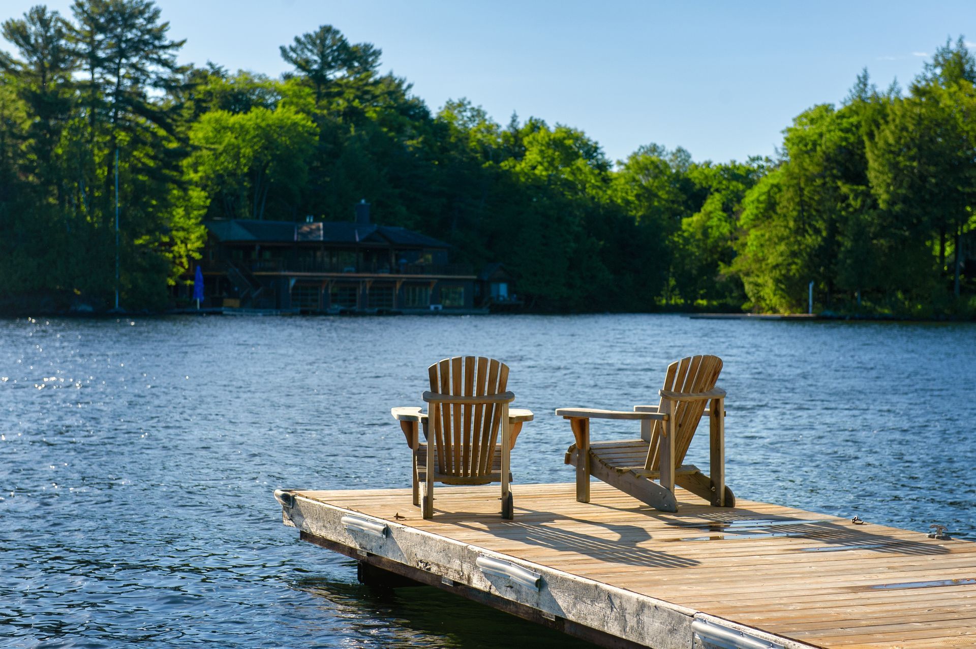 Two wooden chairs on a dock overlooking a calm lake with trees along the shore
