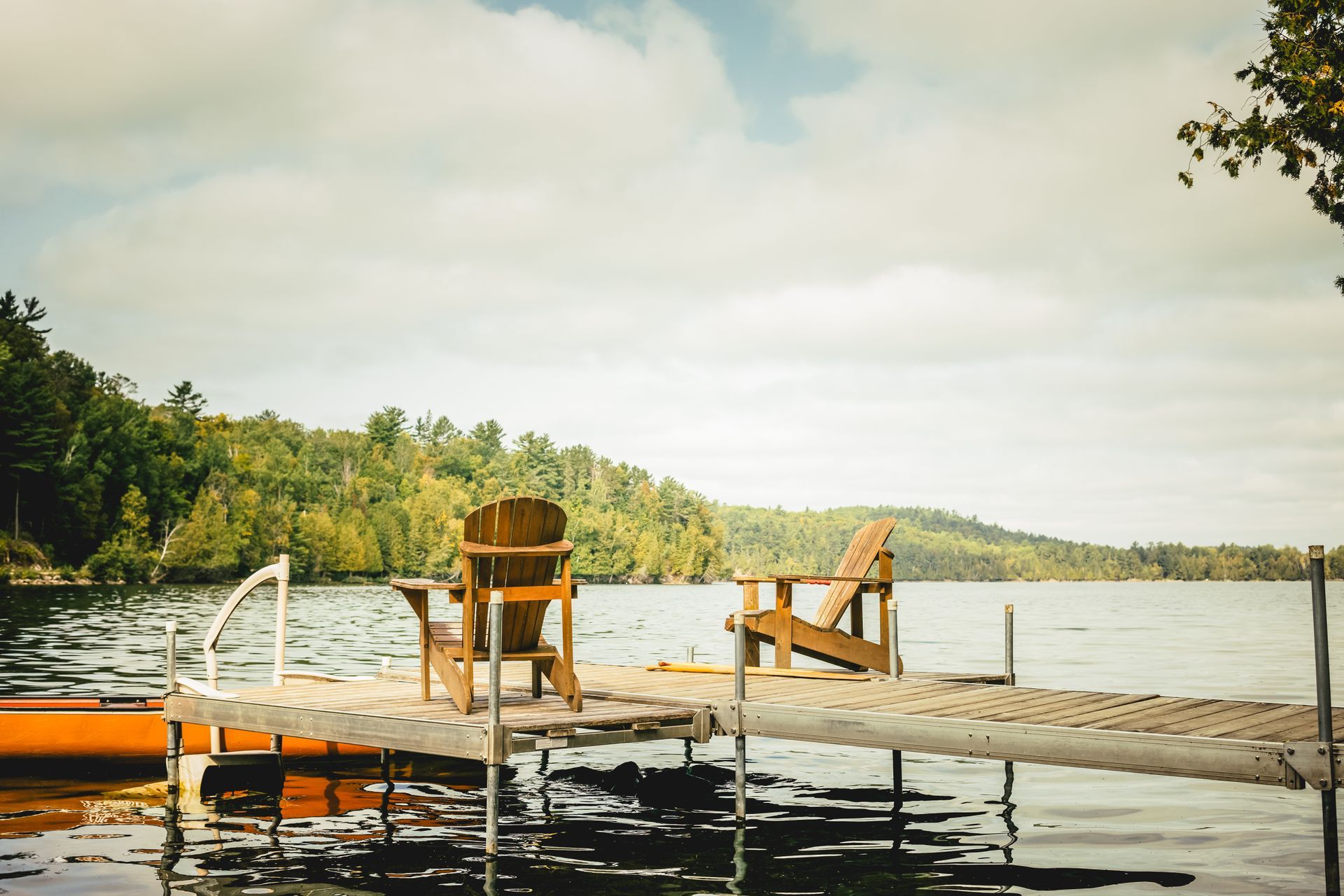Two wooden chairs on a dock over calm lake water at sunset, with trees along the shore