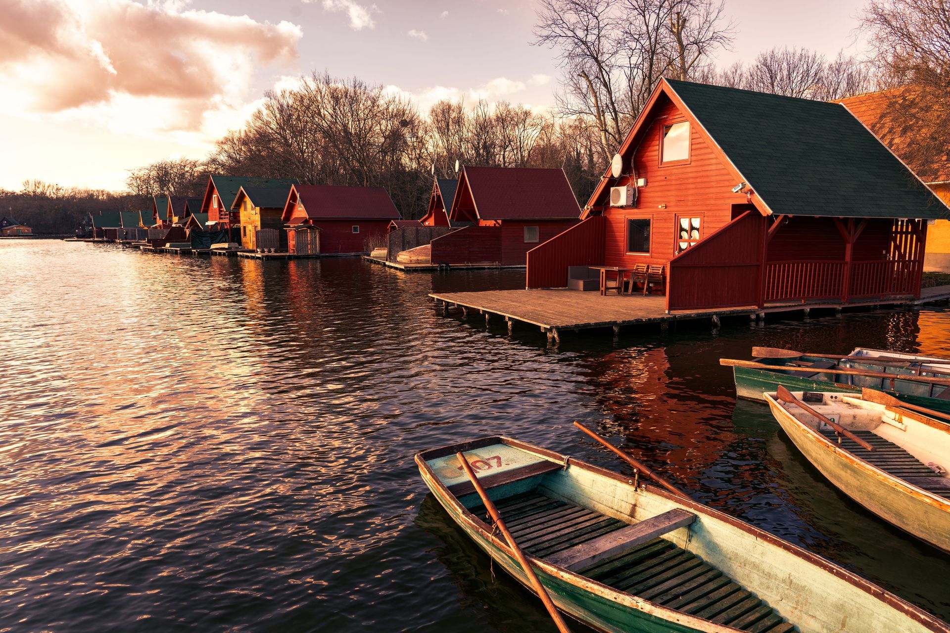 Red lakeside cabins at sunset with boats tied along calm water