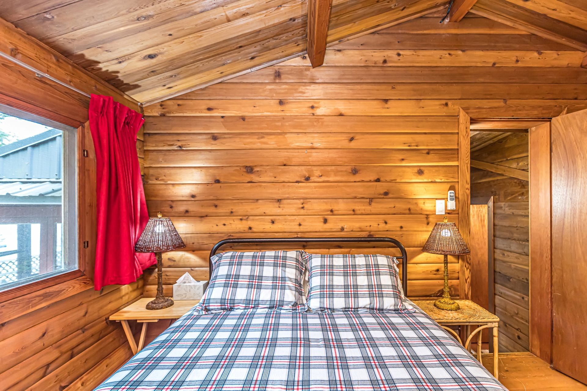Cozy wooden cabin bedroom with plaid bedspread, red curtains, and bedside lamps