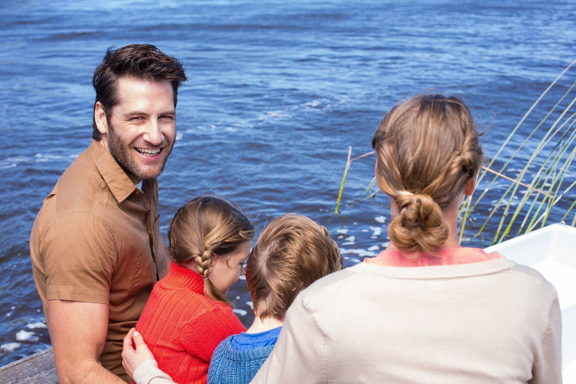 Family on a boat looking at the blue water, with a man smiling toward the camera.