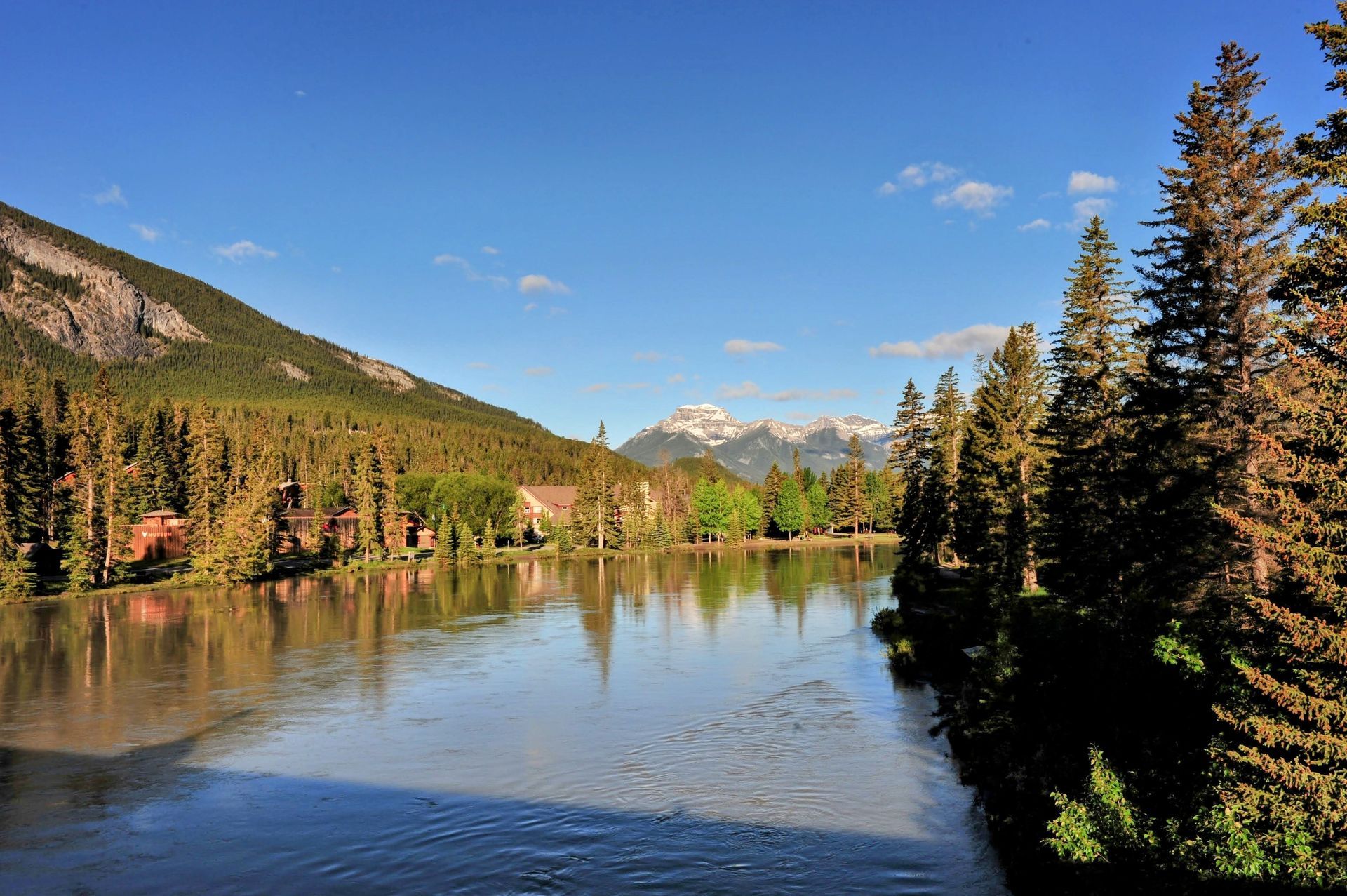 Mountain lake reflecting evergreen trees, with blue sky and distant peaks.