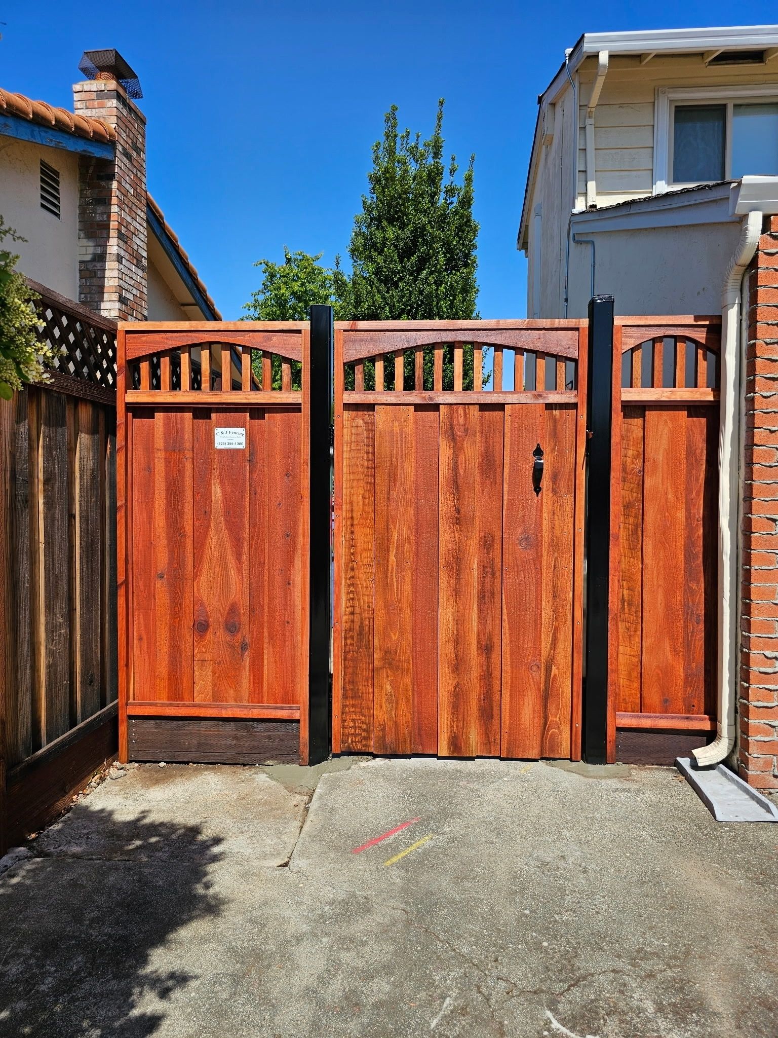 Wooden gate with black posts, leading into a driveway.