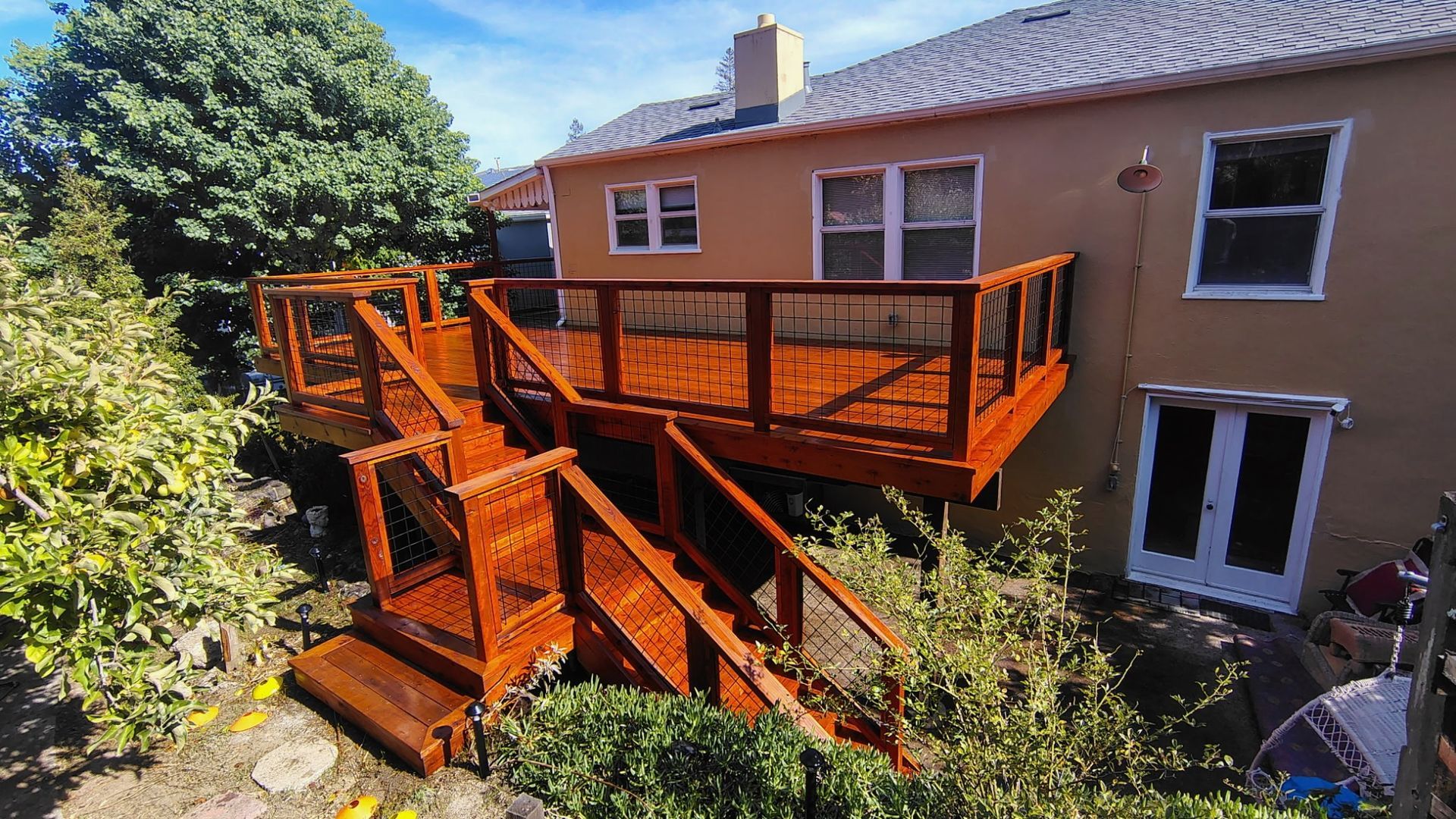 Wooden deck with stairs attached to a two-story house, stained in reddish-brown.
