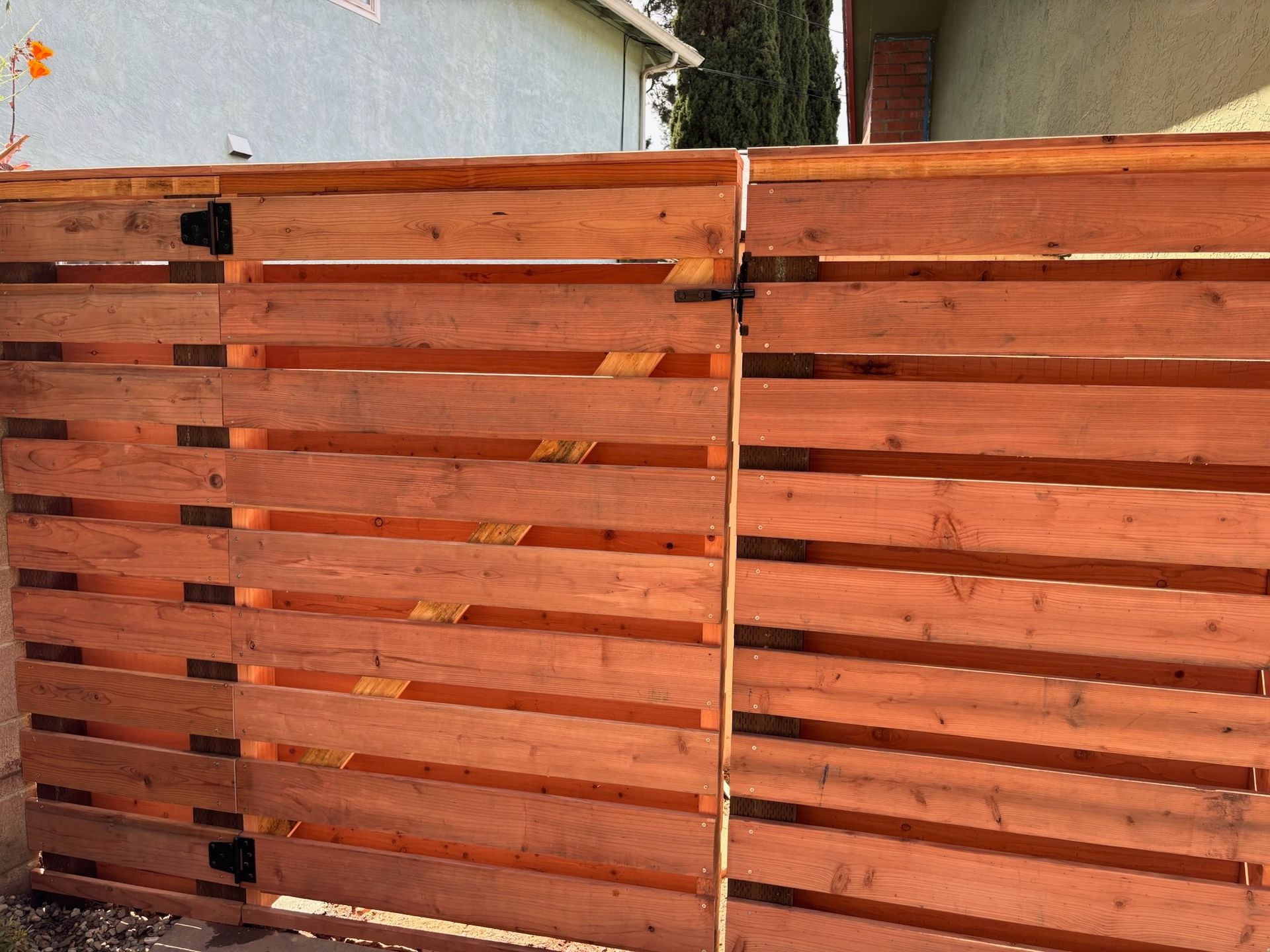 Wooden horizontal slat gate, stained reddish-brown, with black hinges and latch.