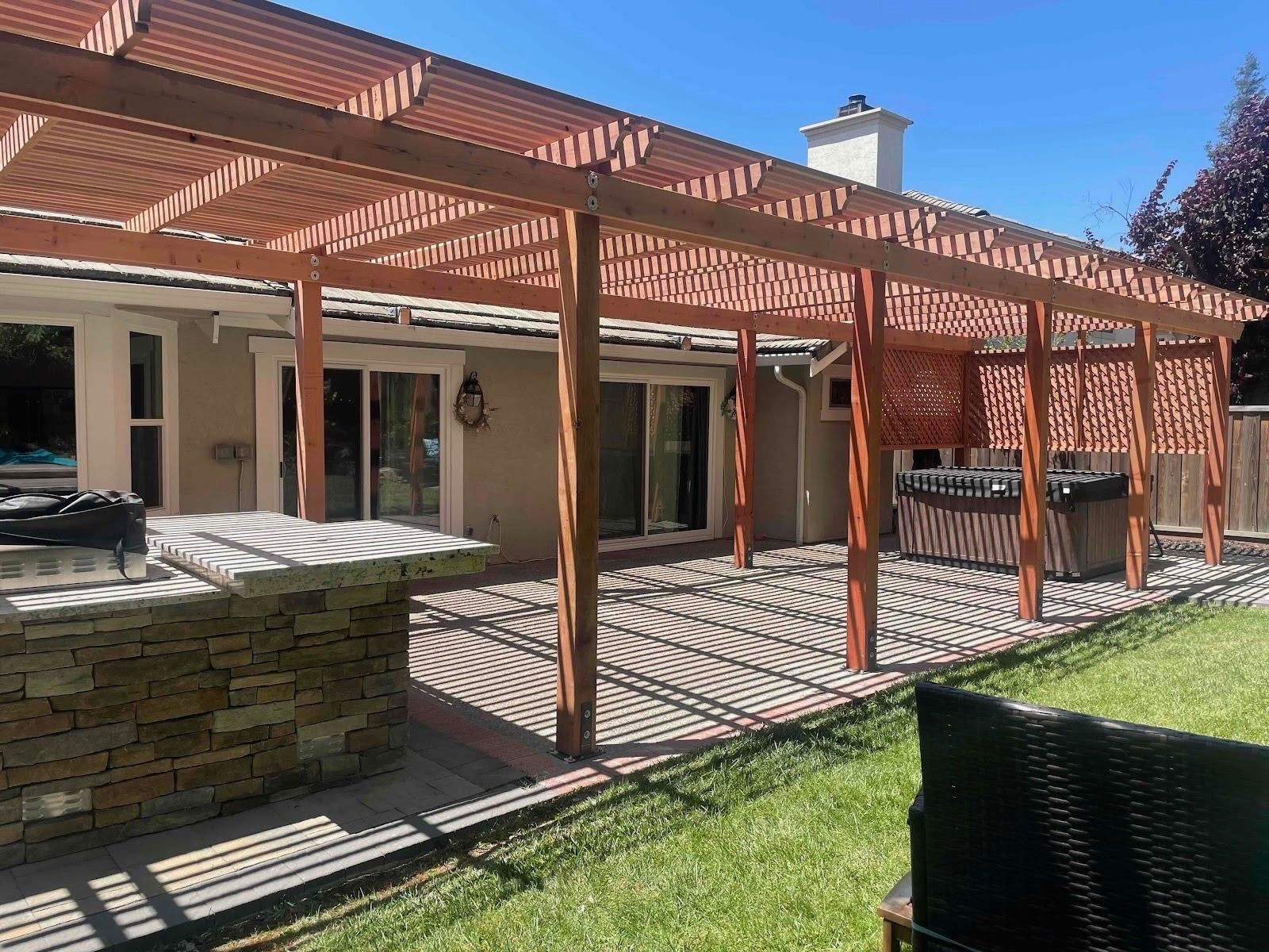 Patio with wooden pergola, brick patio, and hot tub; sunny day.