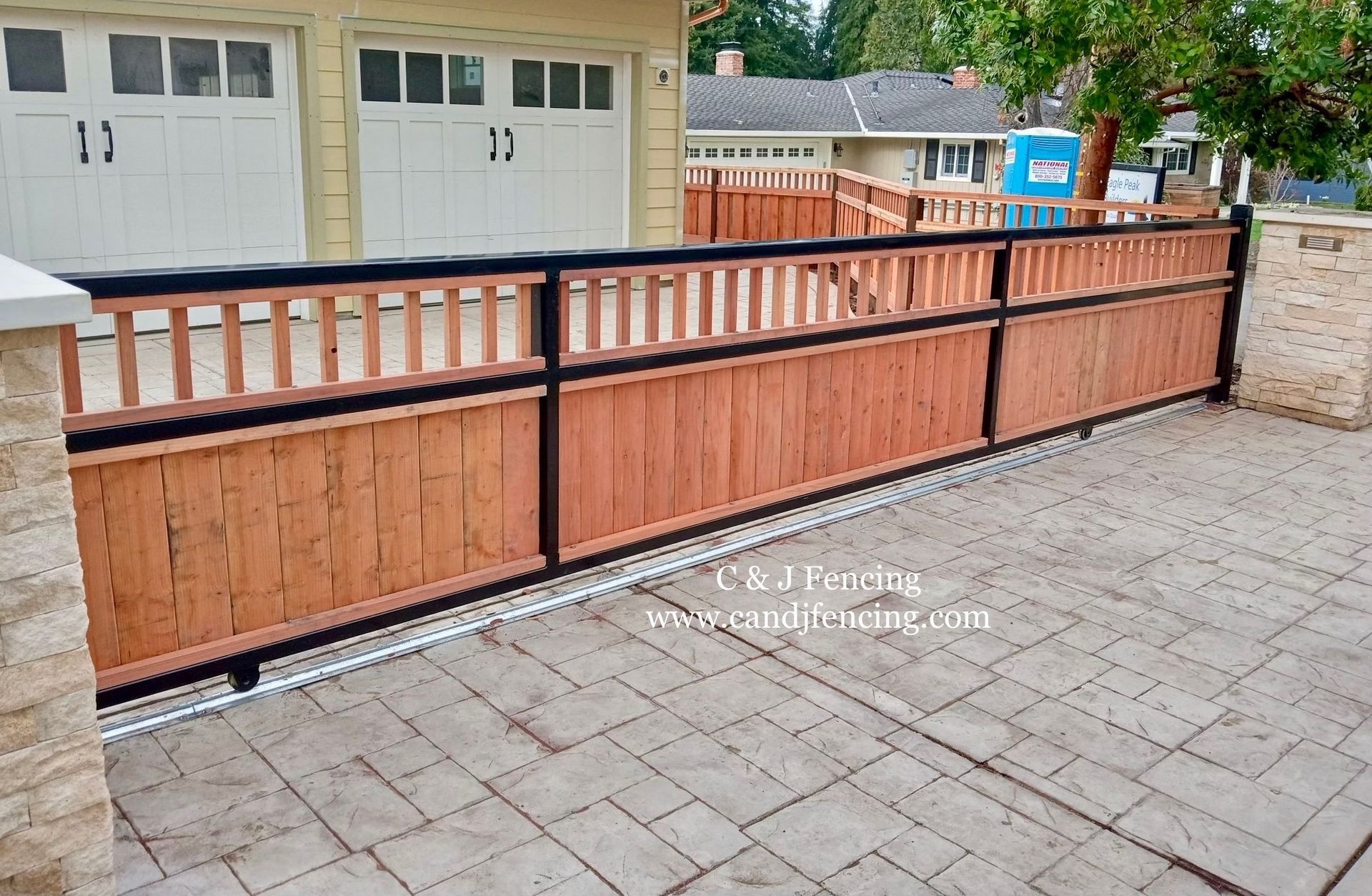 Wooden and black metal driveway gate with wooden fence panels; paved driveway in front of a garage.