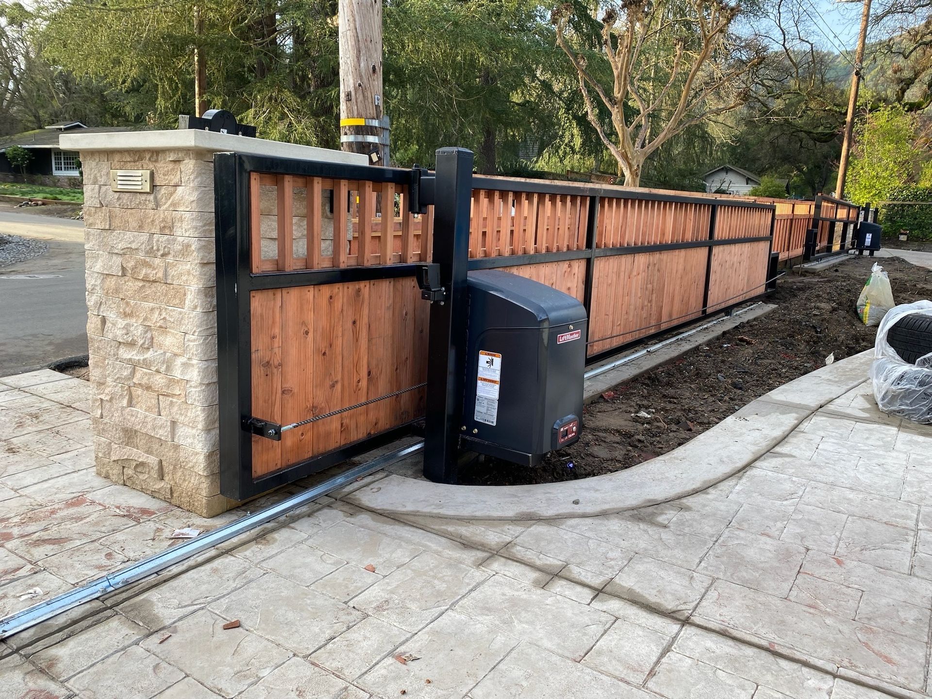 Automatic sliding wooden gate with black frame, brick pillar, and black motor.