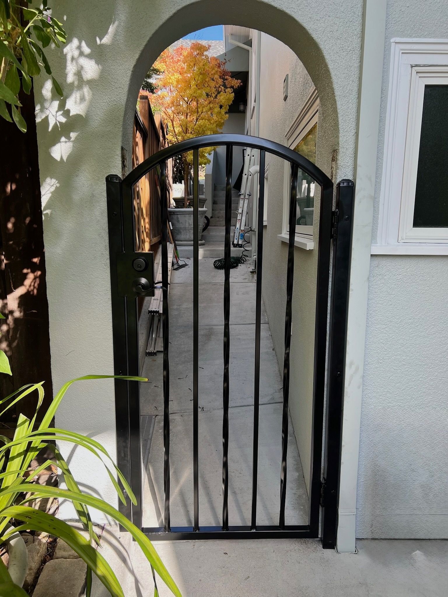 Black metal gate in an arched entryway. Narrow walkway between buildings, autumn leaves visible at the end.