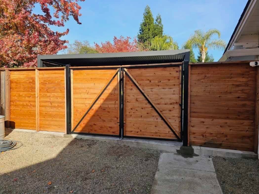 Wooden gate and fence with black metal frame. Sunny outdoor setting.