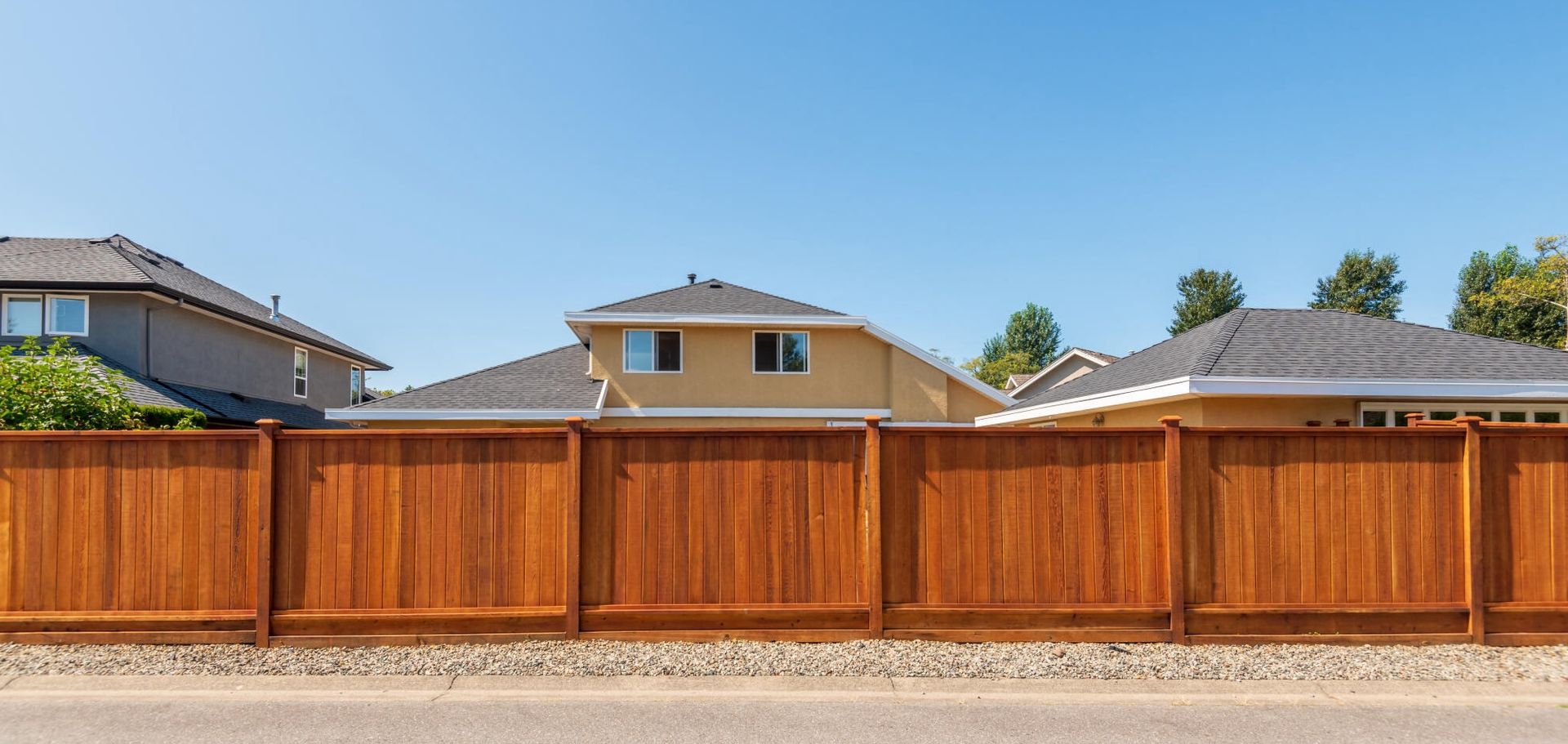 A wooden fence surrounds a residential area with houses in the background.Why Choose Redwood Fencing? Discover Its Advantages