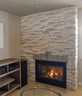 Fireplace with light grey stone, lit fire, surrounded by beige walls, and a glass-top table.