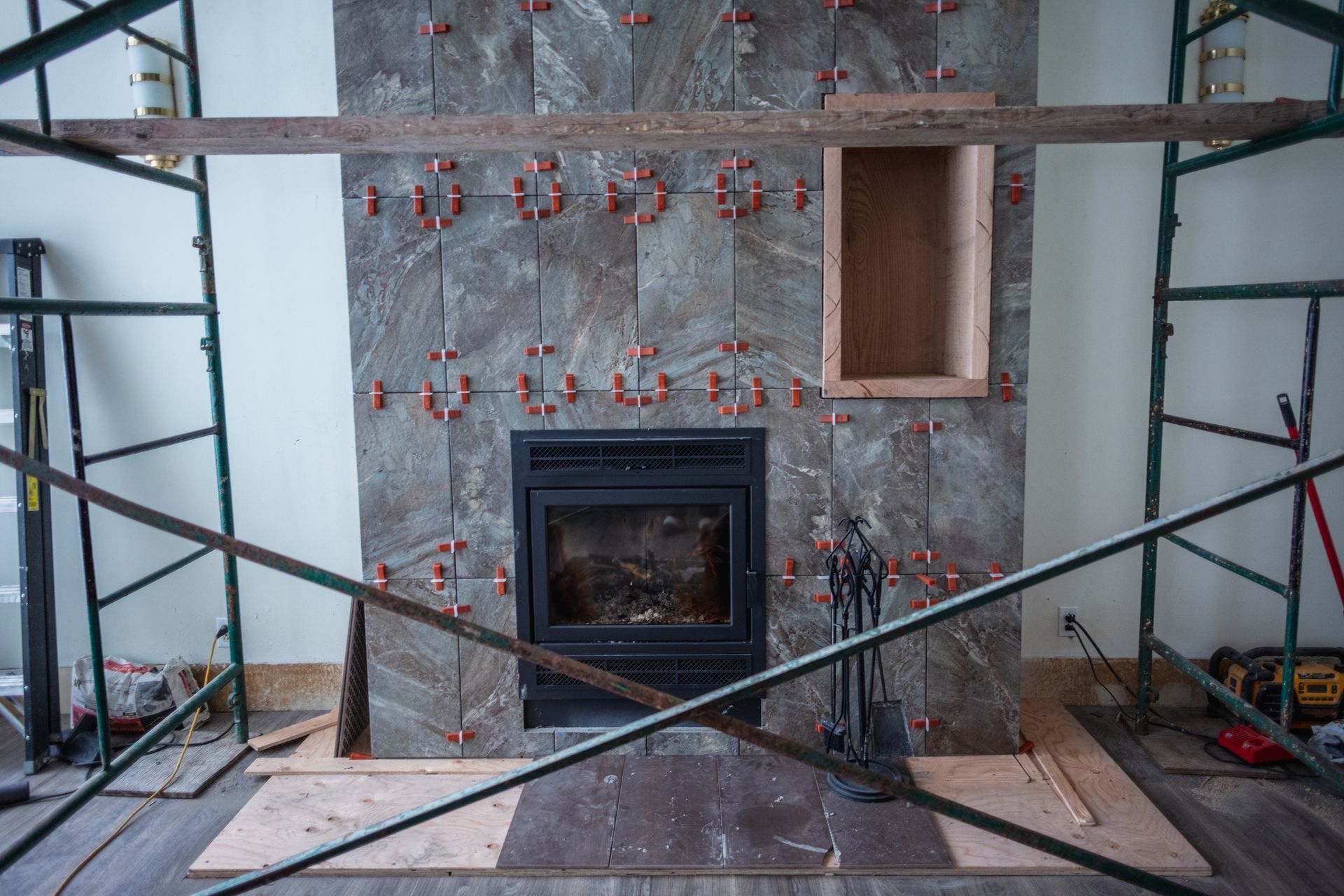 Fireplace being tiled, with fireplace insert installed. Scaffolding surrounds the work in progress.