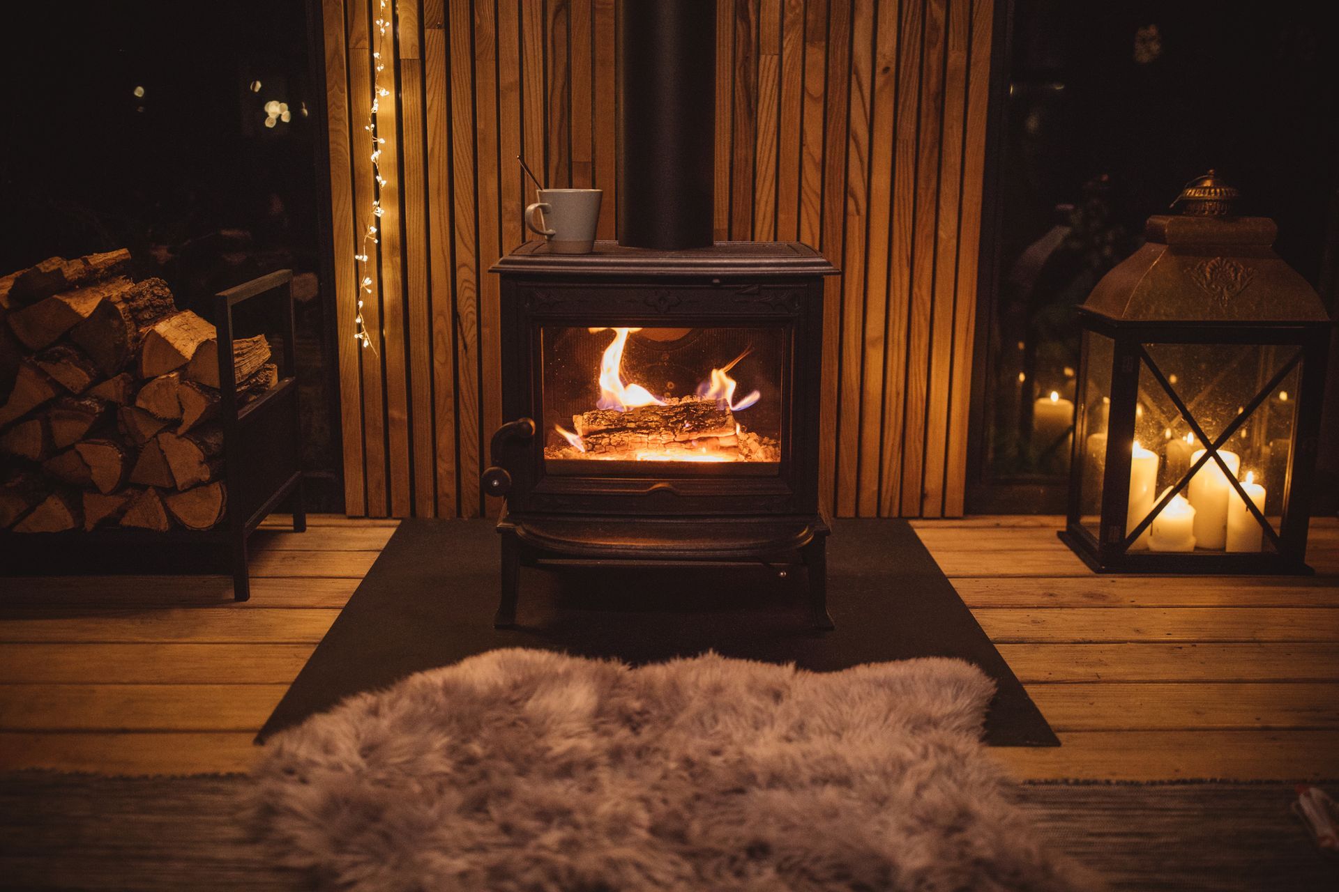 Cozy cabin interior with fireplace, burning logs, sheepskin rug, and lantern.