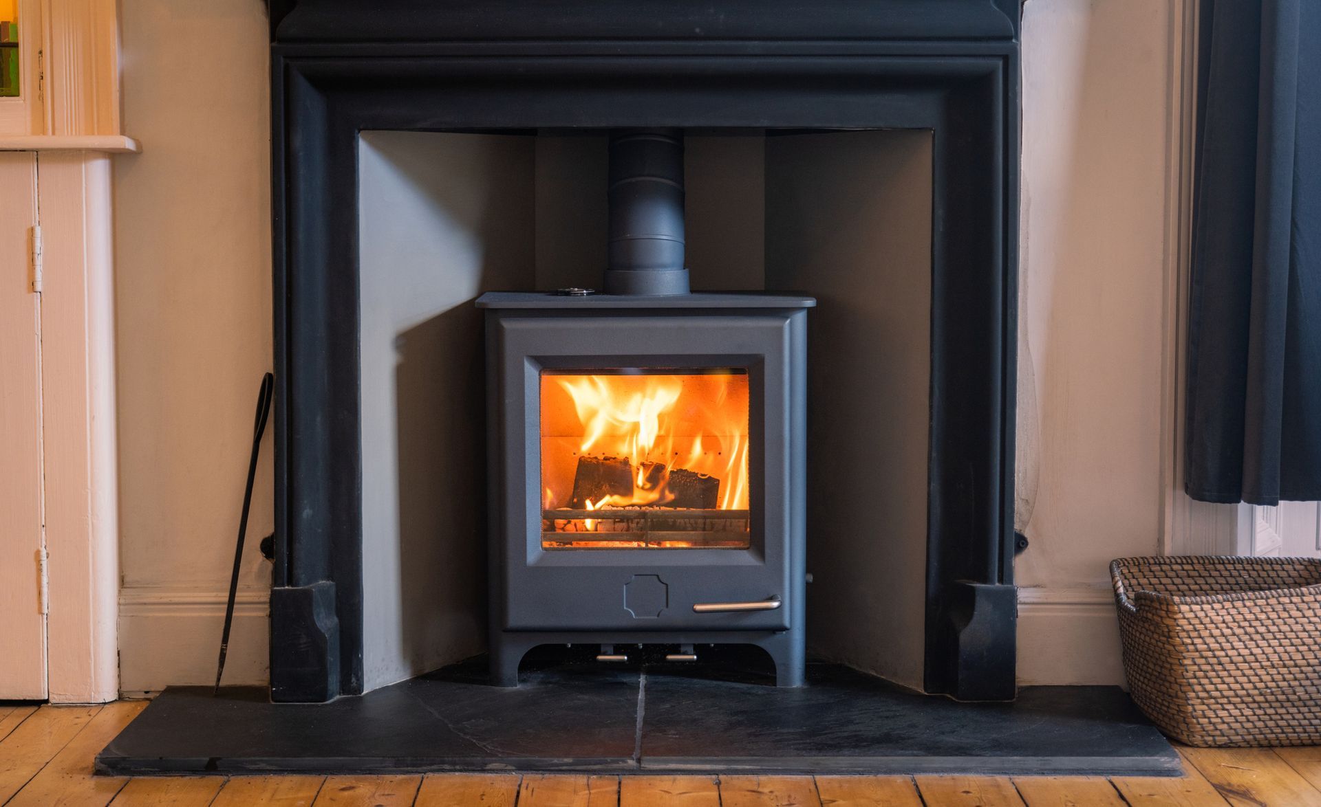 A wood-burning stove with flames inside a fireplace, set against a wall.