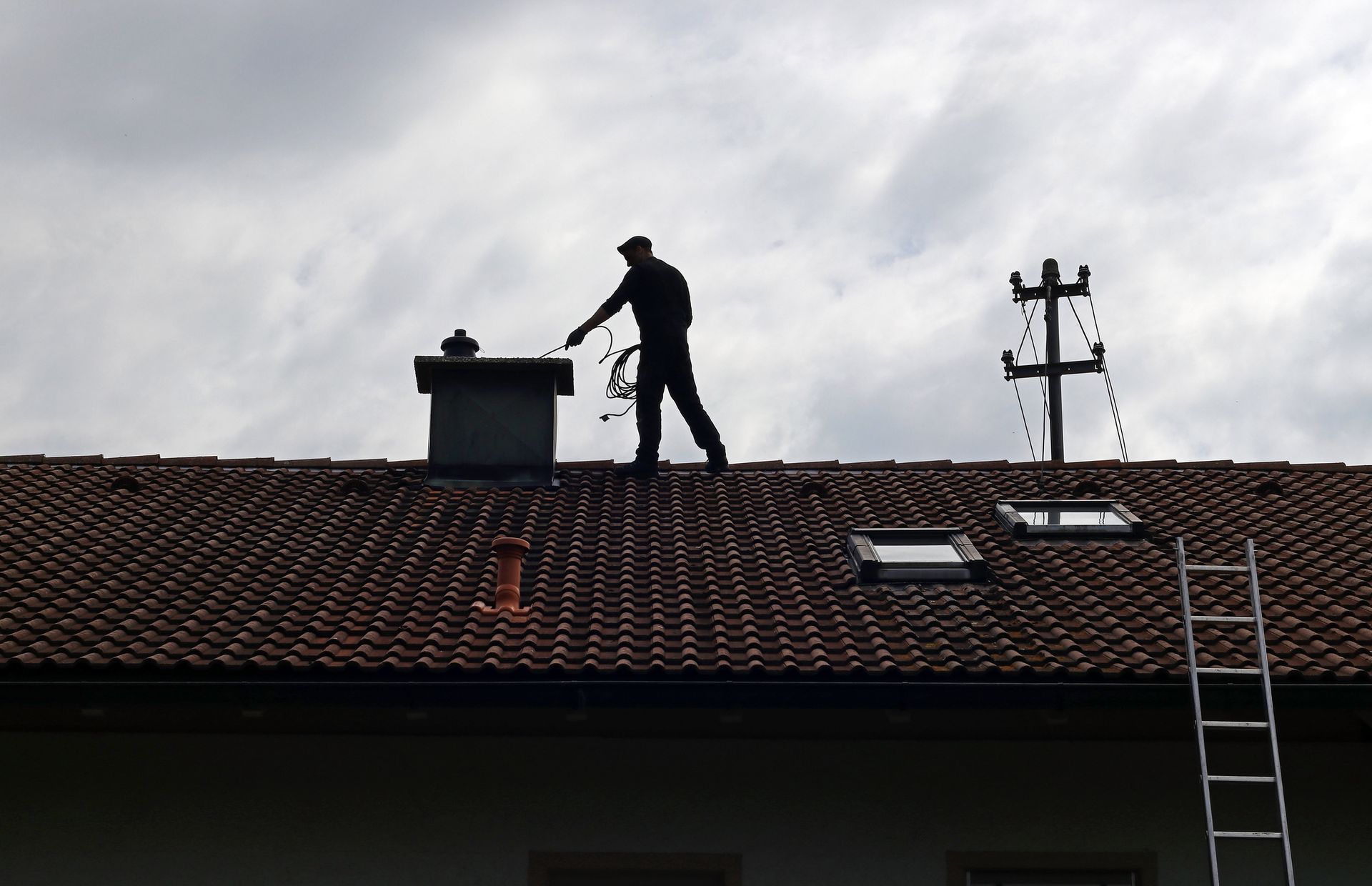 Silhouette of a chimney sweep on a rooftop, cleaning a chimney; cloudy sky overhead.