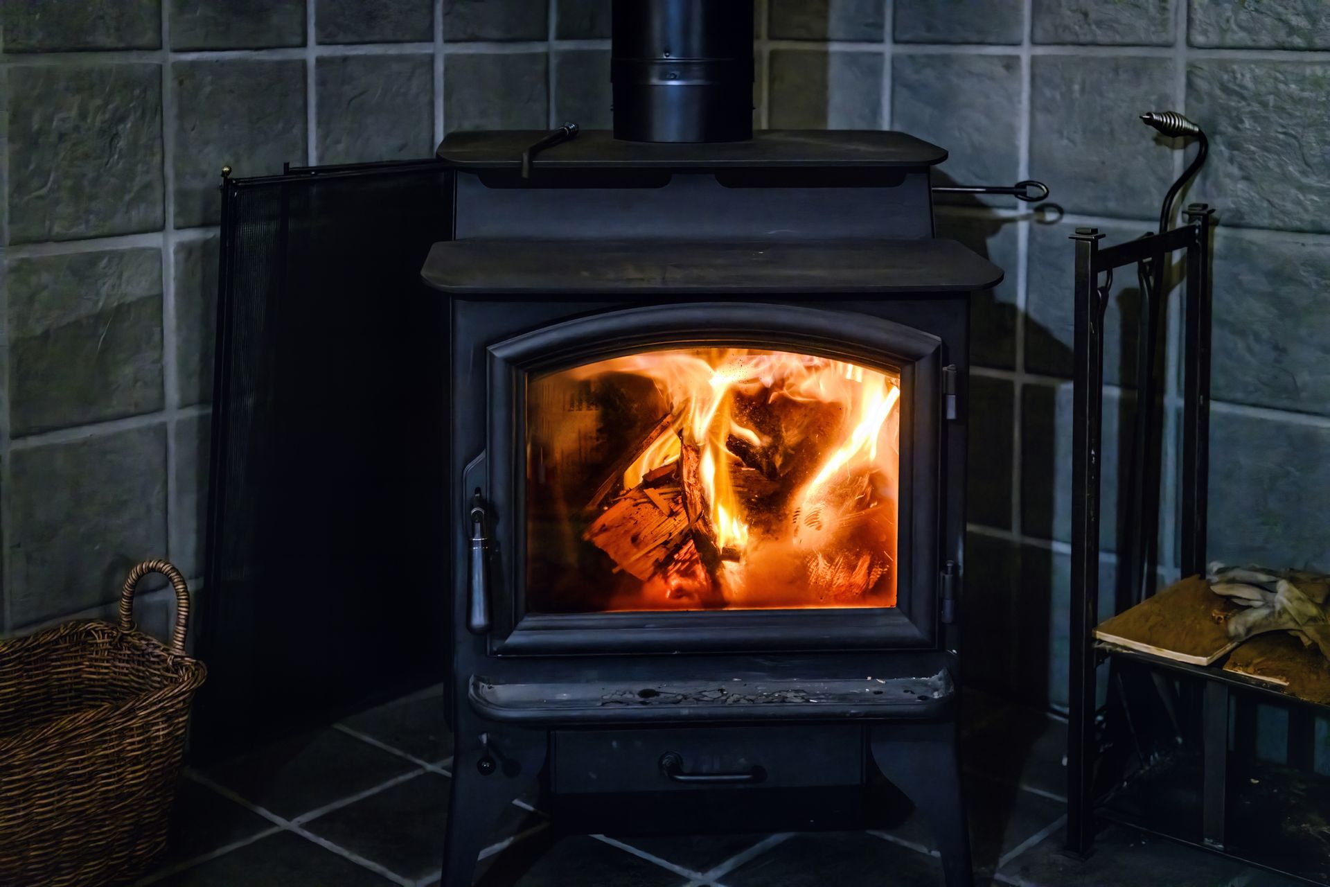 Wood-burning stove with flames inside, against a tiled wall.