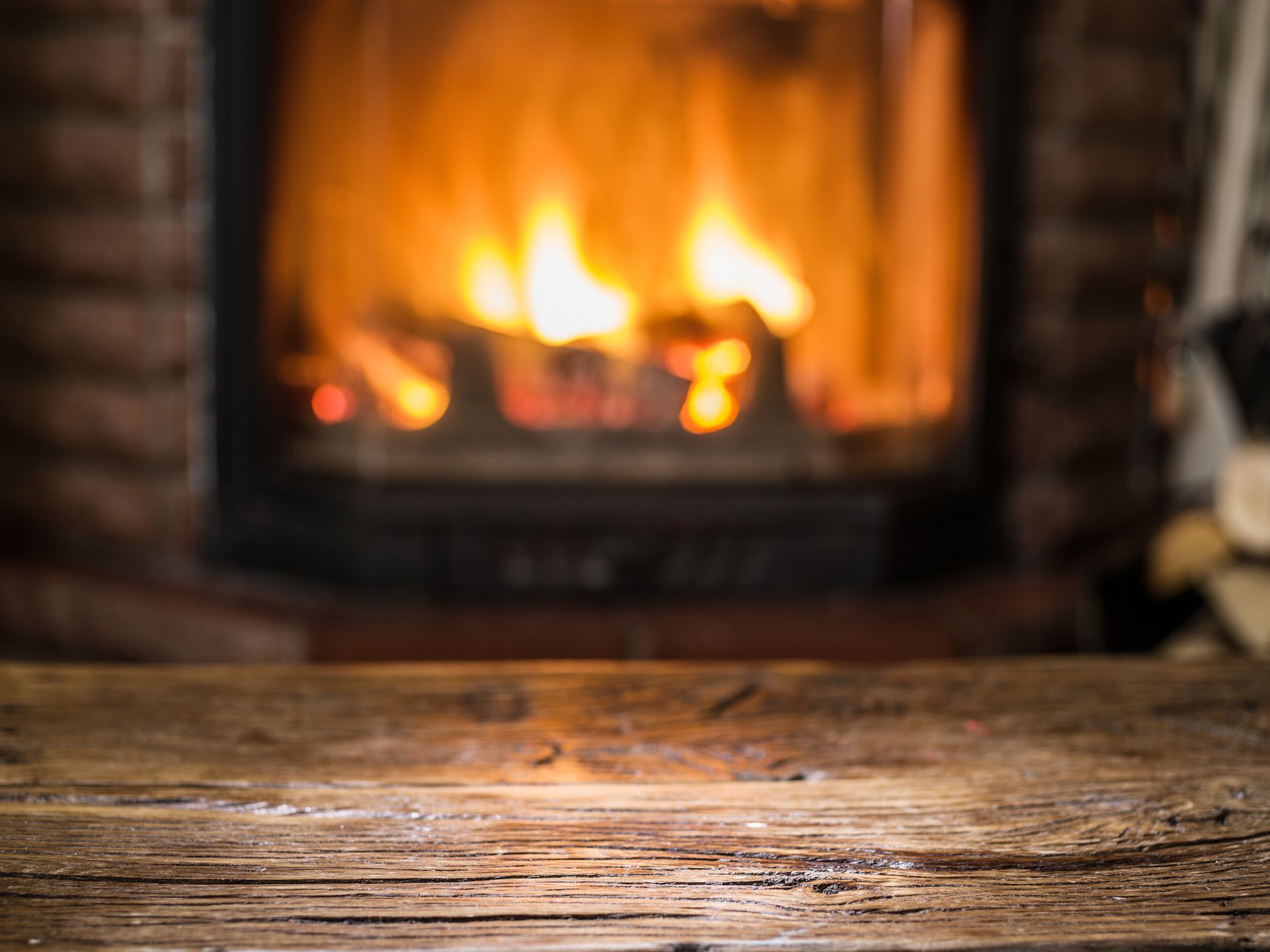 Rustic wooden table in front of a warm fireplace with bright orange flames.