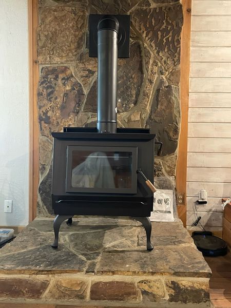 Black wood-burning stove with metal chimney against a stone wall.