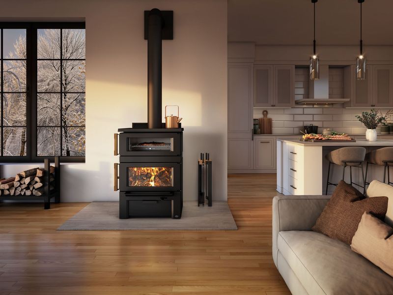 A cozy living room with a lit wood stove. Sunlight streams through a window, illuminating a kitchen.