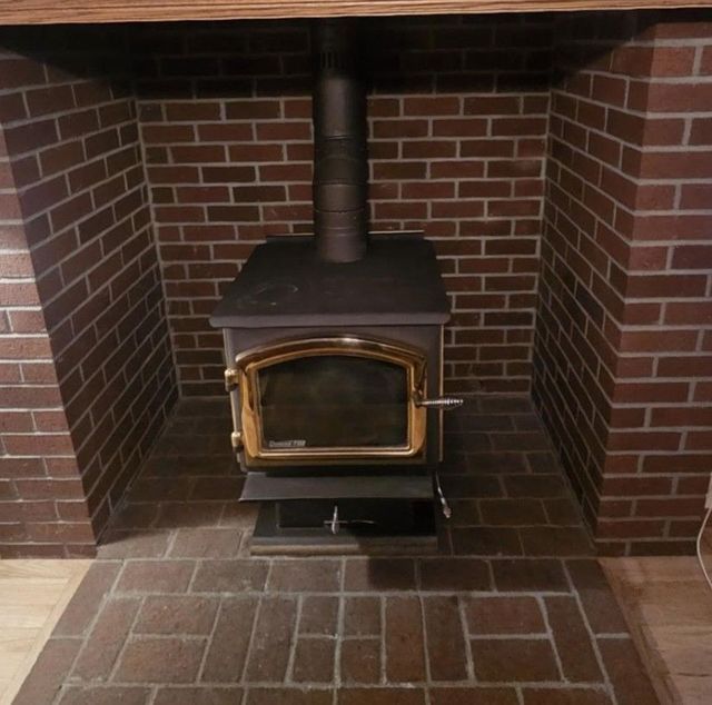 Wood-burning stove inside brick fireplace with black stove pipe, a brick surround, and hearth.