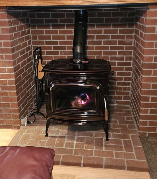 Wood stove inside a brick fireplace. Black stove with glowing embers, black chimney.