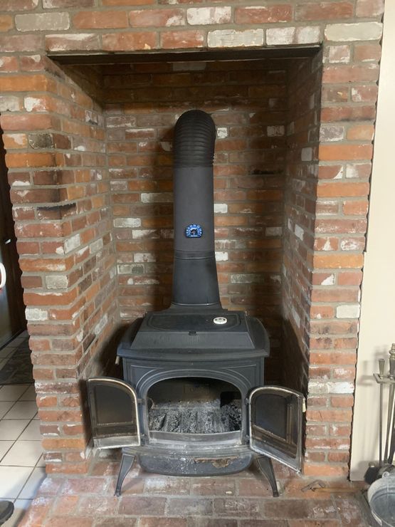 Wood stove with open doors inside a red brick fireplace.