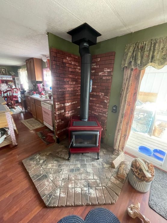 A red wood-burning stove with a black chimney in a corner with a brick surround, on a brick hearth.