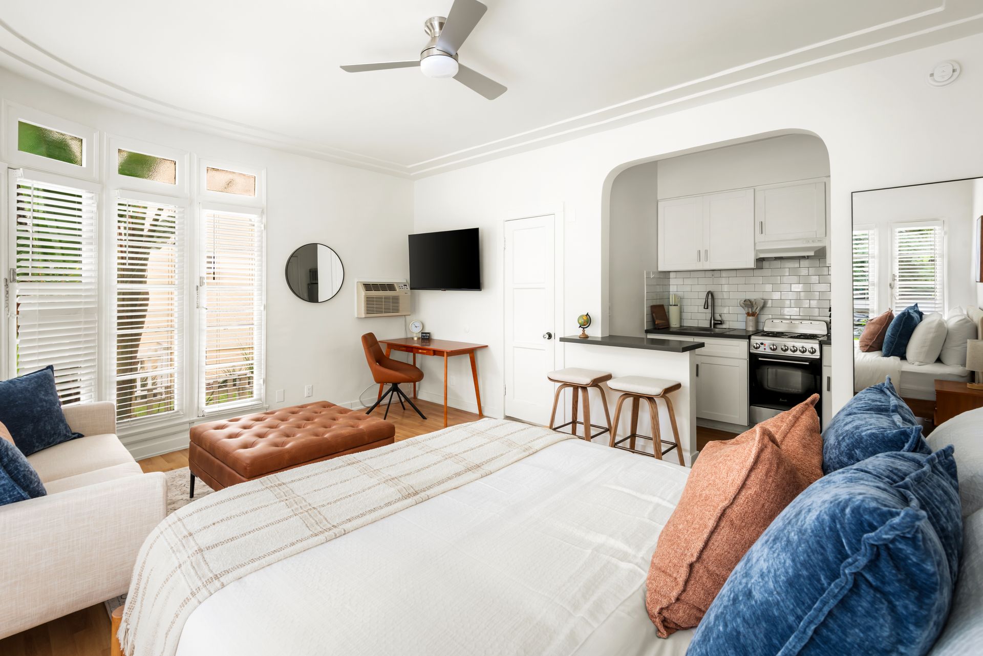 Small studio apartment with bed, kitchenette, and seating area. White walls, wood floors, and natural light.