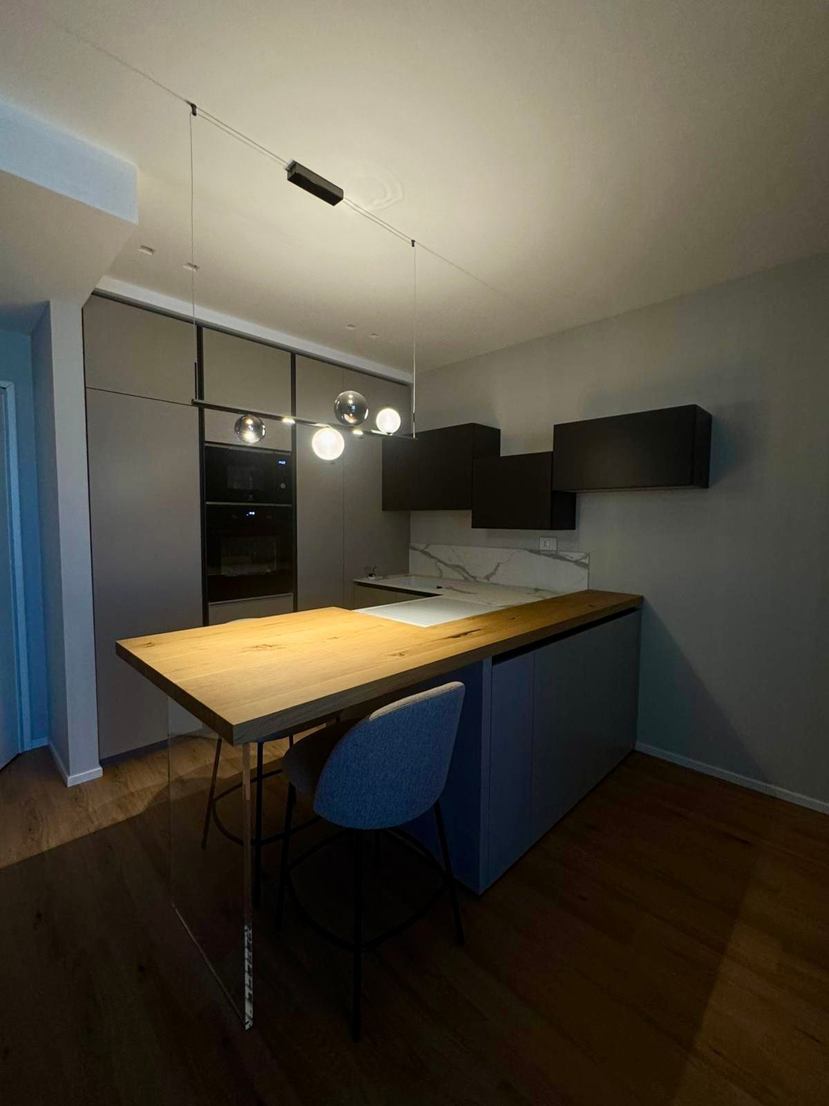 Cucina moderna con tavolo in legno, mobili grigi e lampada a sospensione.