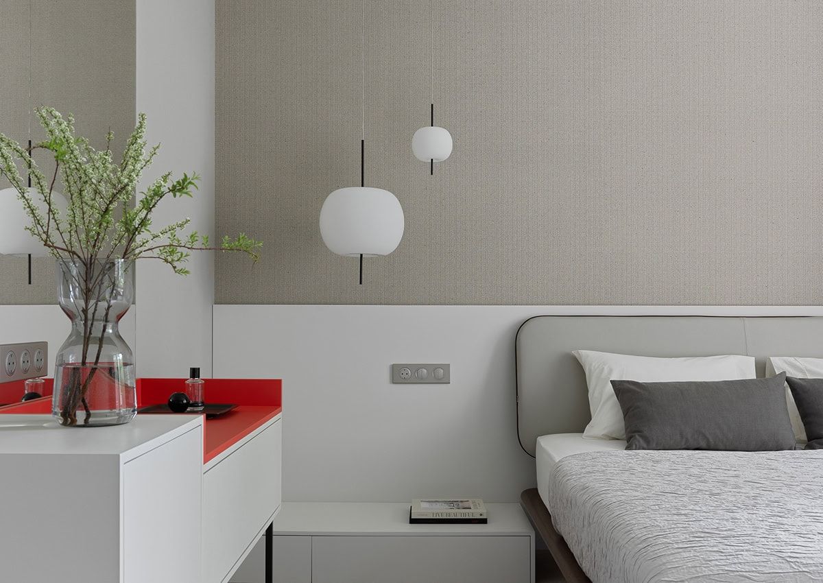 Camera da letto con letto, comodino, mobili a muro bianchi e rossi, vaso decorativo e lampade a sospensione contro una parete strutturata.