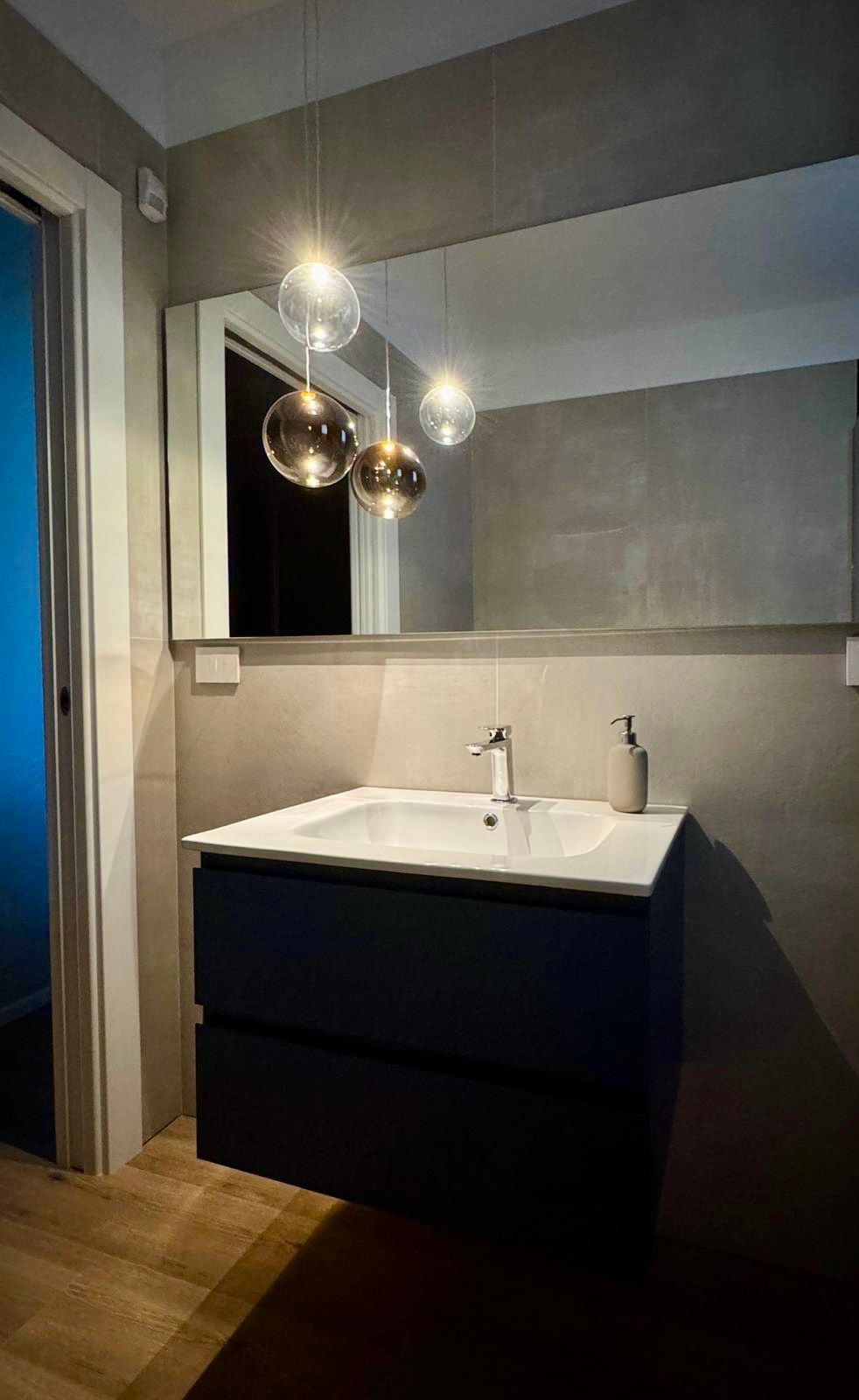 Mobiletto del bagno con mobiletto blu, specchio rettangolare e tre lampade a sospensione.