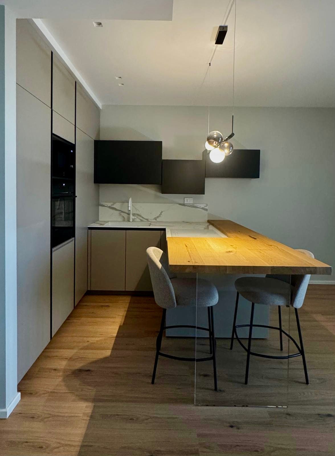 Cucina moderna con isola in legno, mobili neri e due sgabelli da bar.