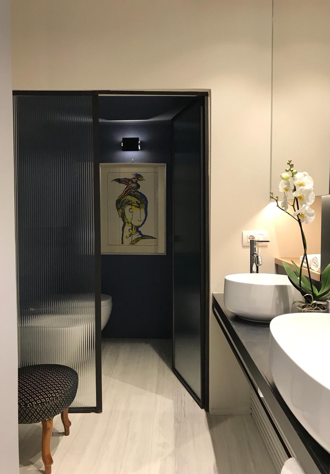 Interno del bagno: una piccola zona toilette con cornice nera e porta in vetro testurizzato; all'interno sono visibili delle opere d'arte.