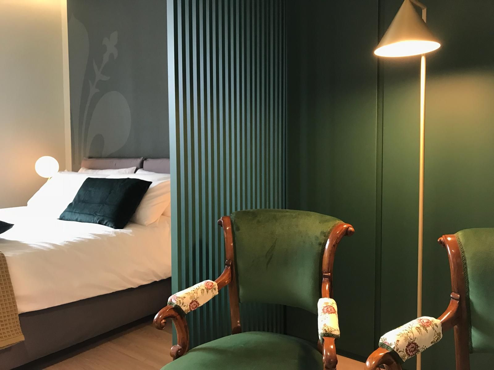 Poltrone in velluto verde con braccioli decorati, accanto a una camera da letto con un letto bianco e una parete verde.