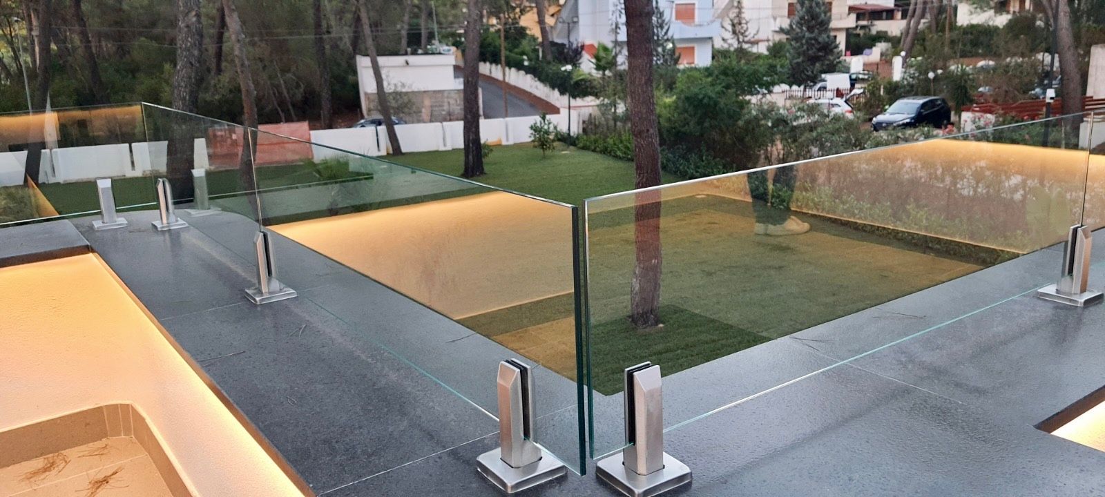 Un moderno patio esterno con ringhiera in vetro che si affaccia su un prato e sugli alberi.