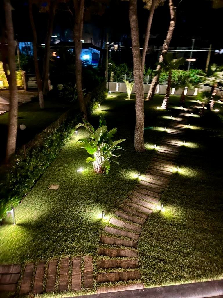 Un sentiero notturno nel giardino illuminato da piccole luci, circondato da alberi e vegetazione.