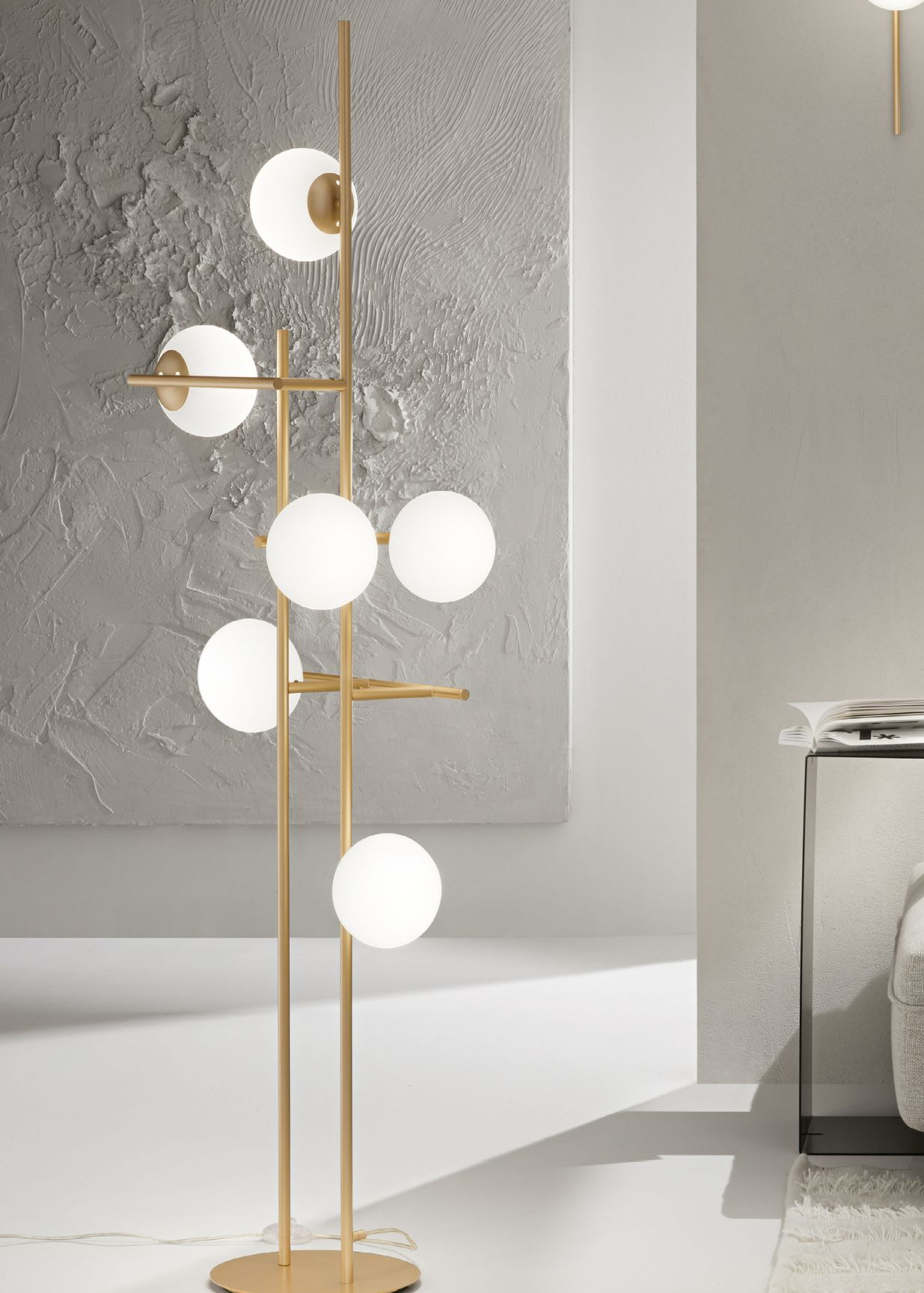 Lampada da terra dorata con luci a globo smerigliate, vicino a una parete strutturata.