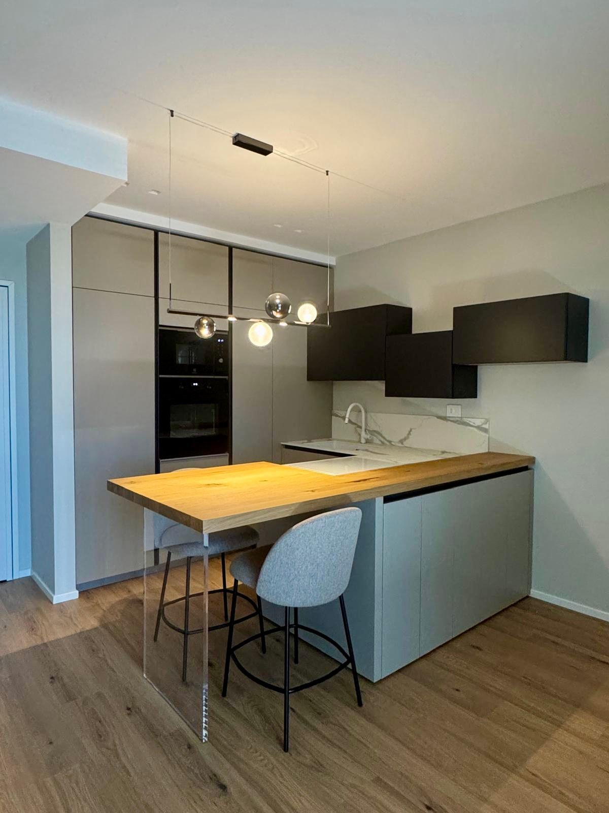 Cucina moderna con isola, tavolo in legno, mobili grigi e lampada a sospensione.