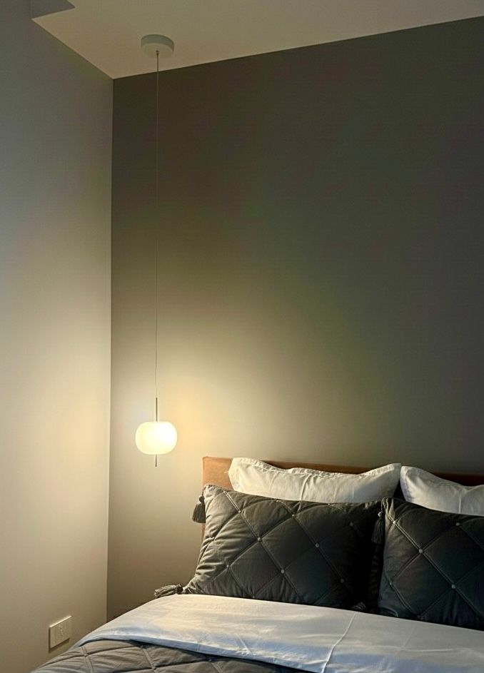 Angolo della camera da letto con lampada a sospensione sopra il letto con cuscini. Pareti grigie, luce soffusa.