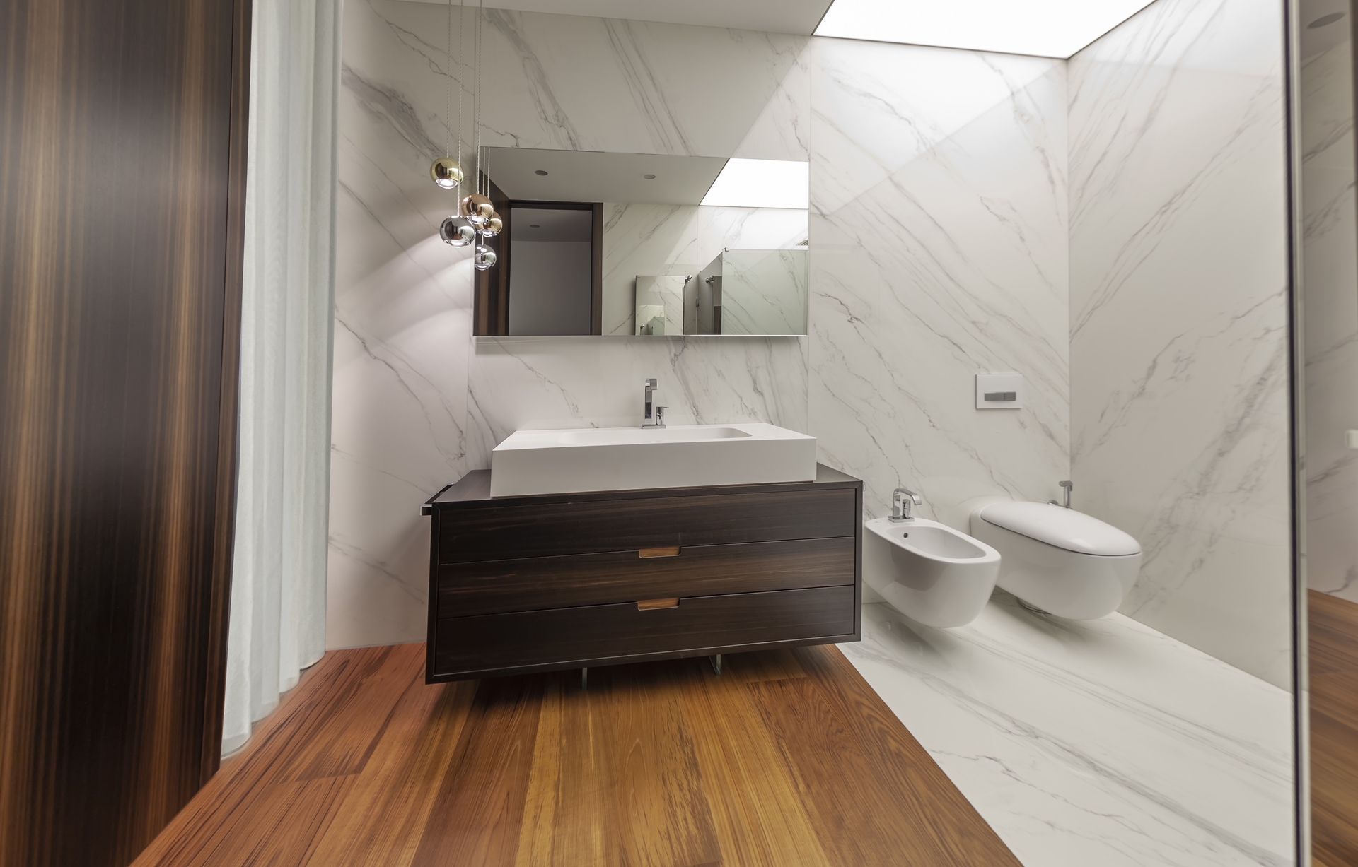 Bagno moderno con pareti in marmo, mobile lavabo in legno e sanitari bianchi.